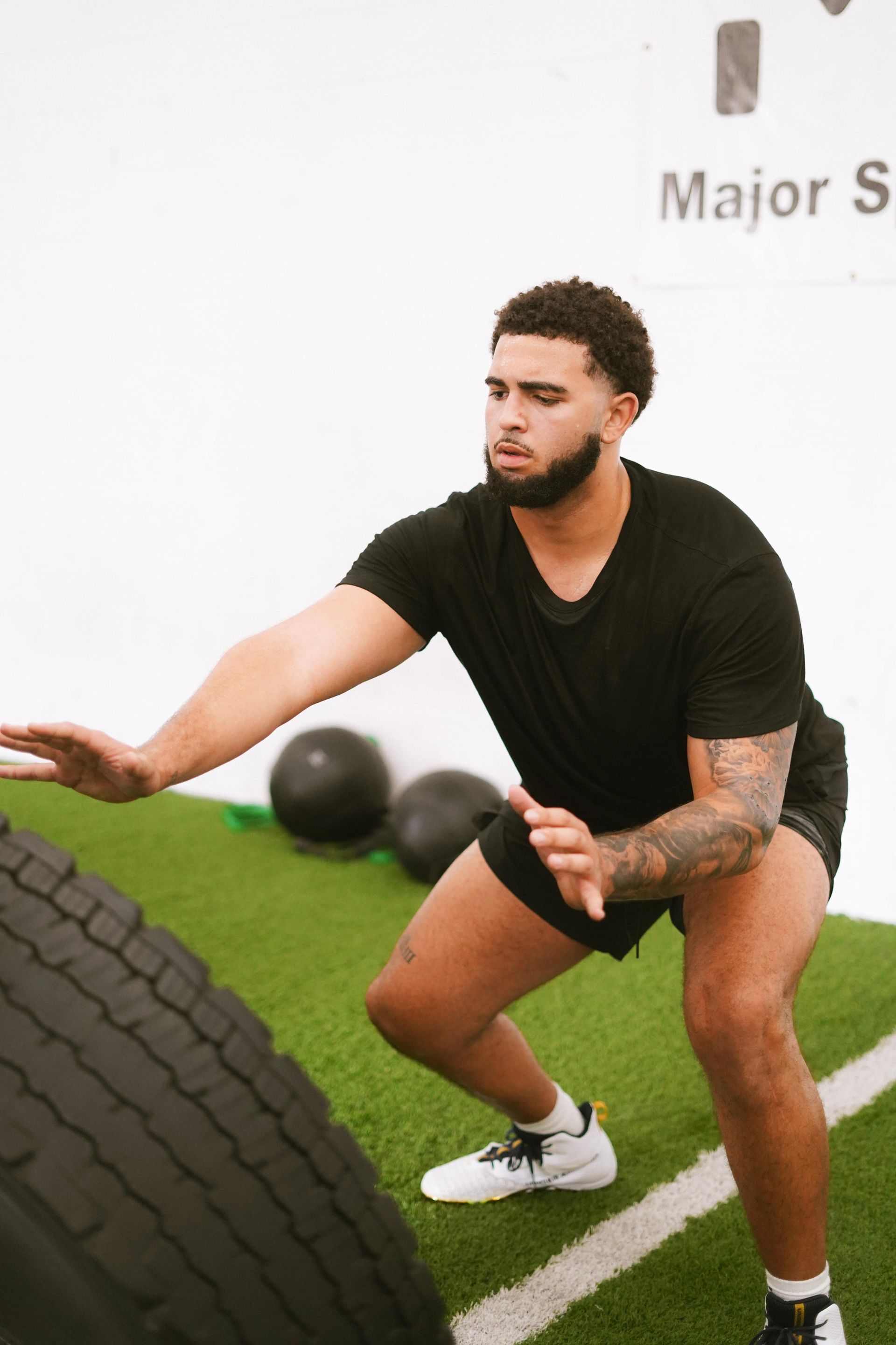 Man in black attire flips a tire at a gym, squatting, intense focus.