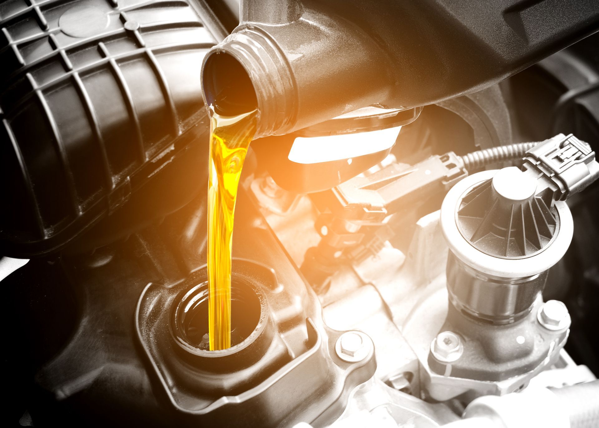 Oil being poured from a container into a car engine, highlighting lubrication process.