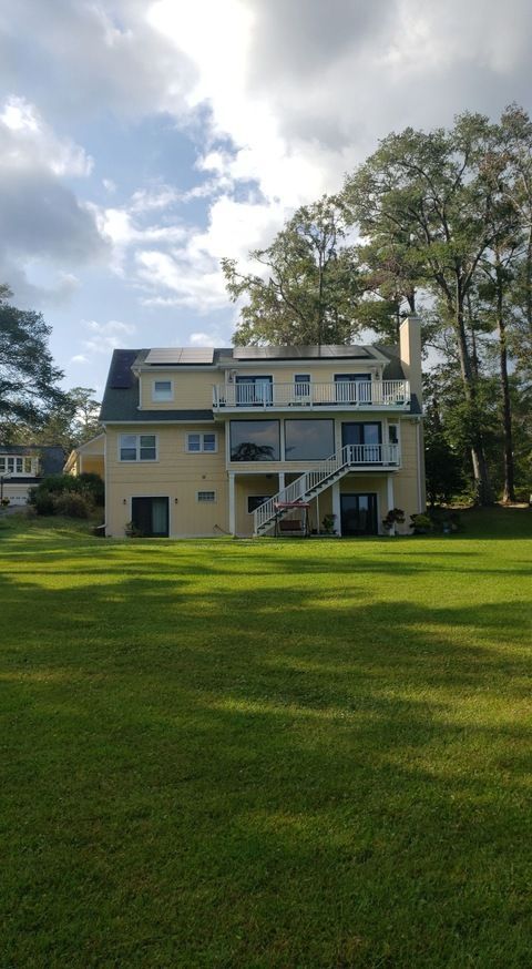 The back of a large house with a large lawn in front of it.