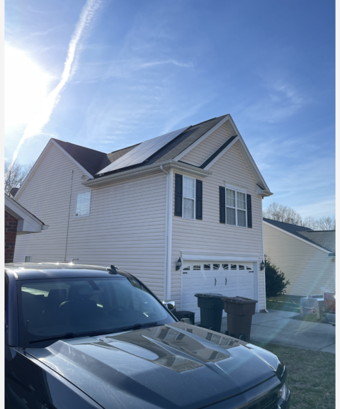 A car is parked in front of a house with solar panels on the roof