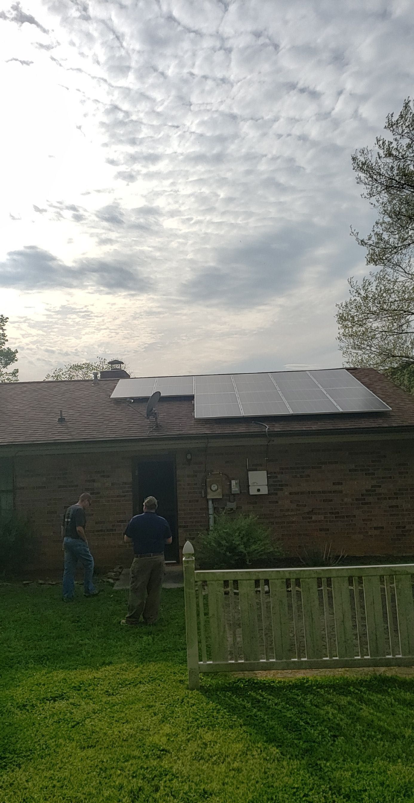 A man is standing in front of a house with solar panels on the roof.
