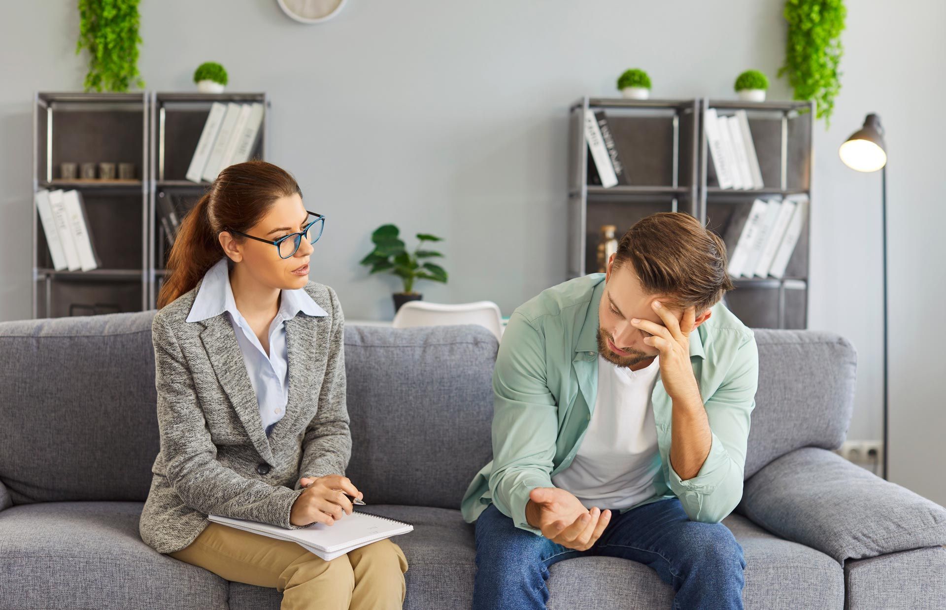 Two people talking on a gray couch in a bright office, one consoling the other who looks upset