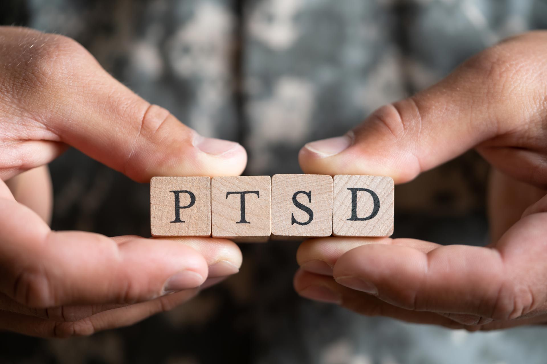 Hands holding wooden blocks spelling PTSD against a blurred background