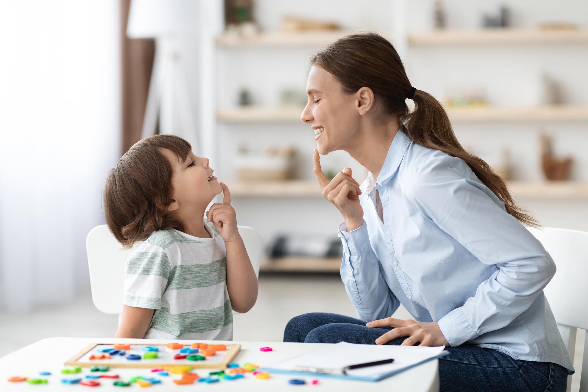 Woman and child smiling at each other while painting at a table with colorful art supplies