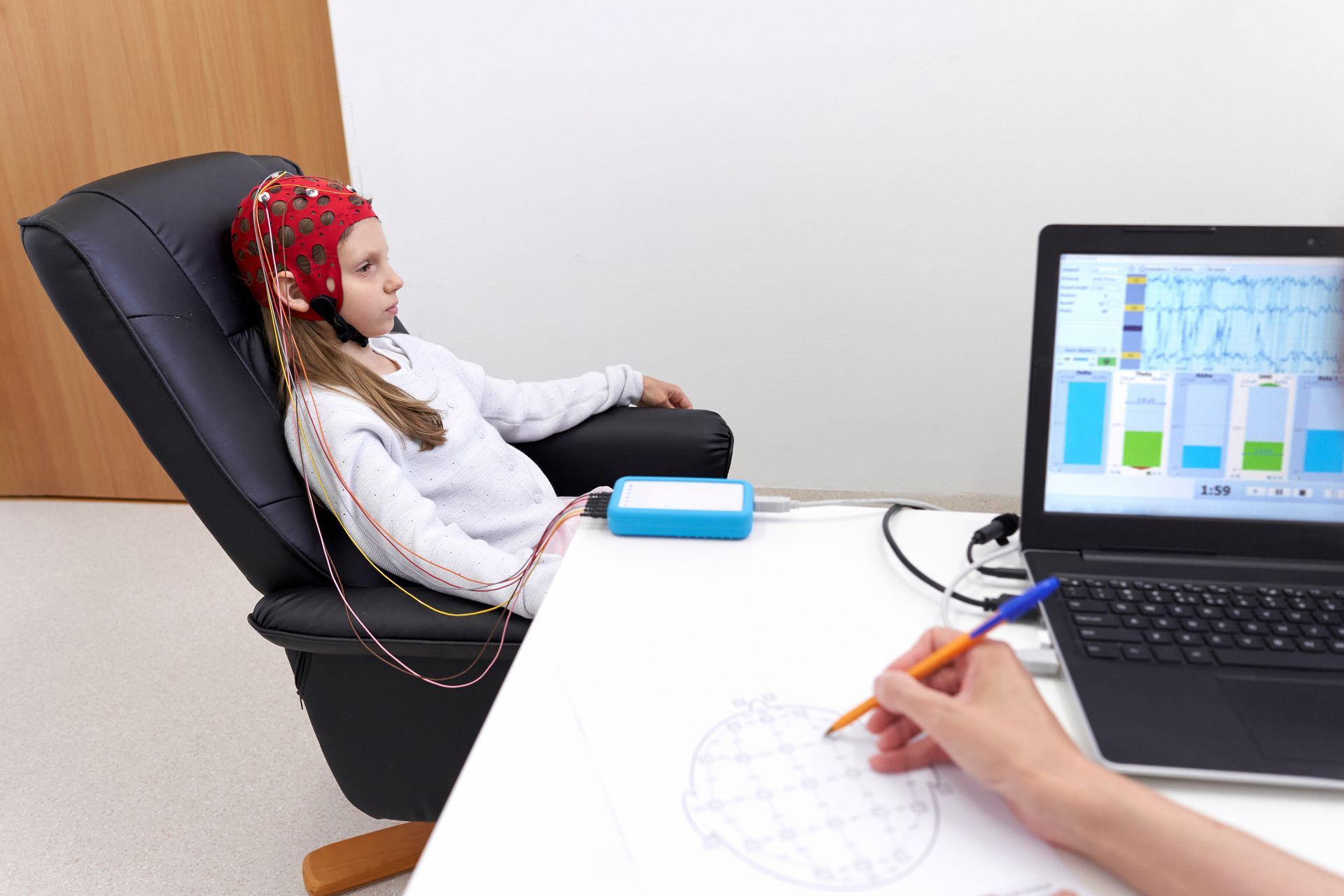 Child reclining in a chair during a clinical test while a clinician records results on a computer