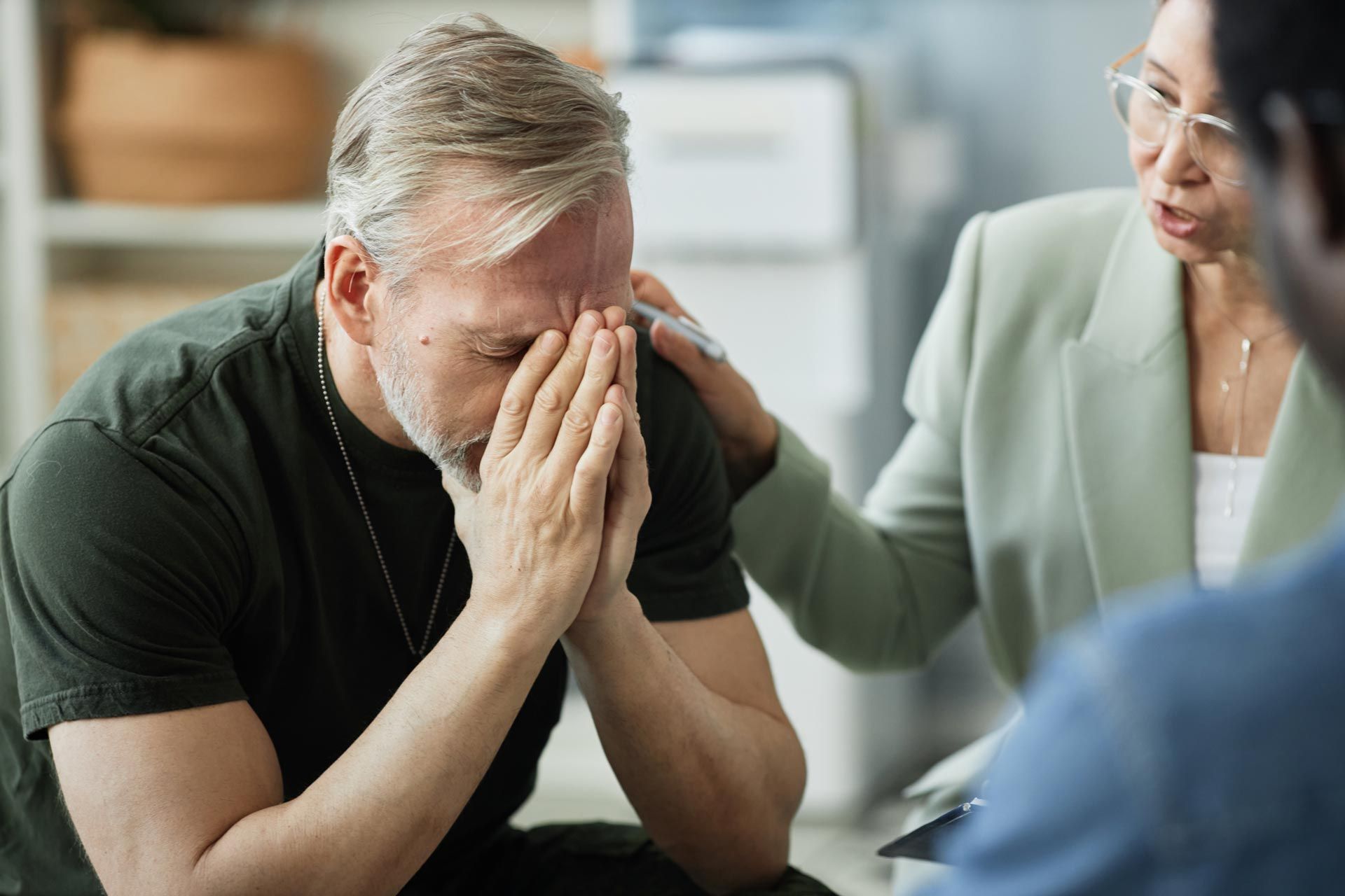 Distressed man holding his face while a counselor comforts him in a therapy session