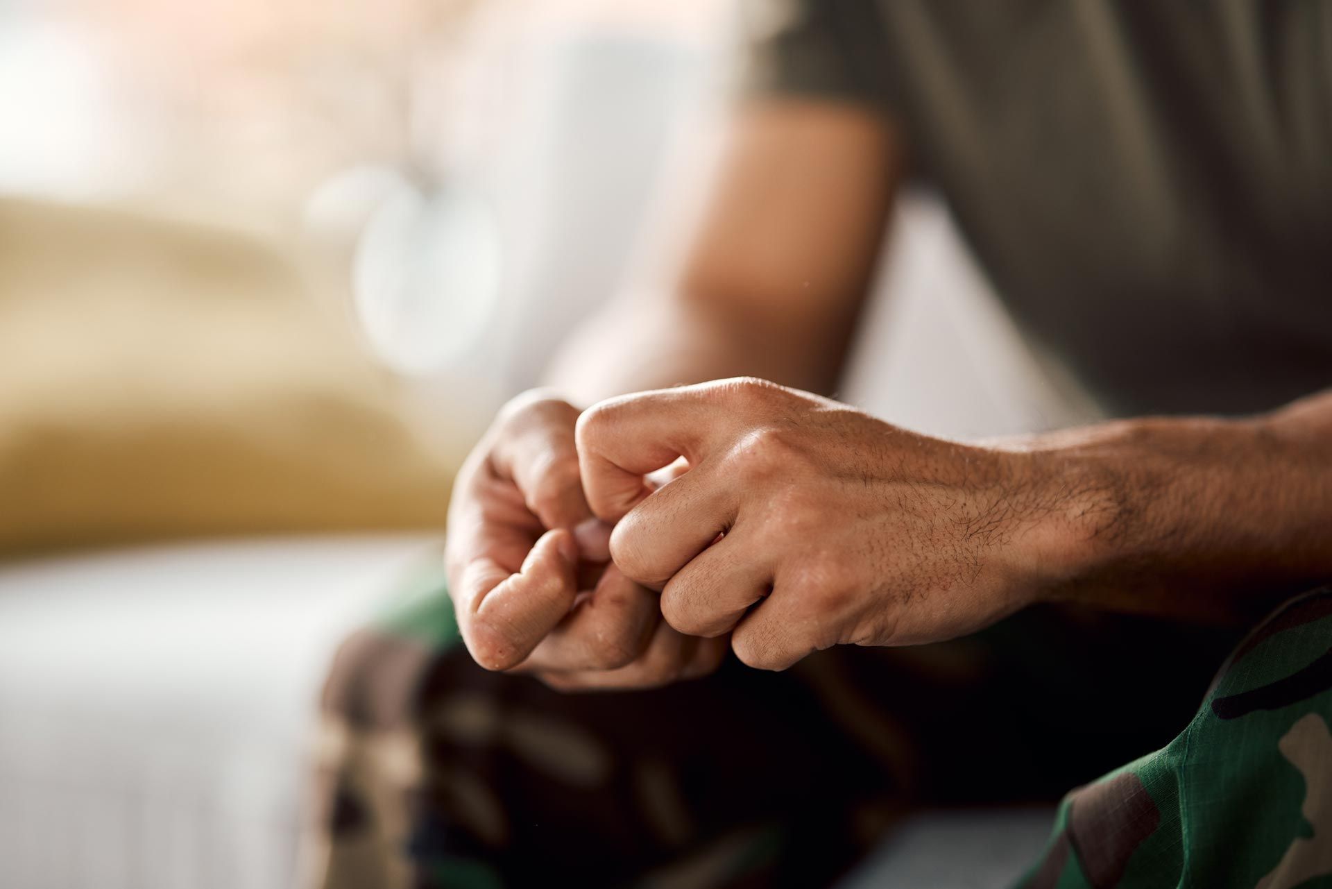 Hands clasped in a seated pose, with a blurred indoor background.