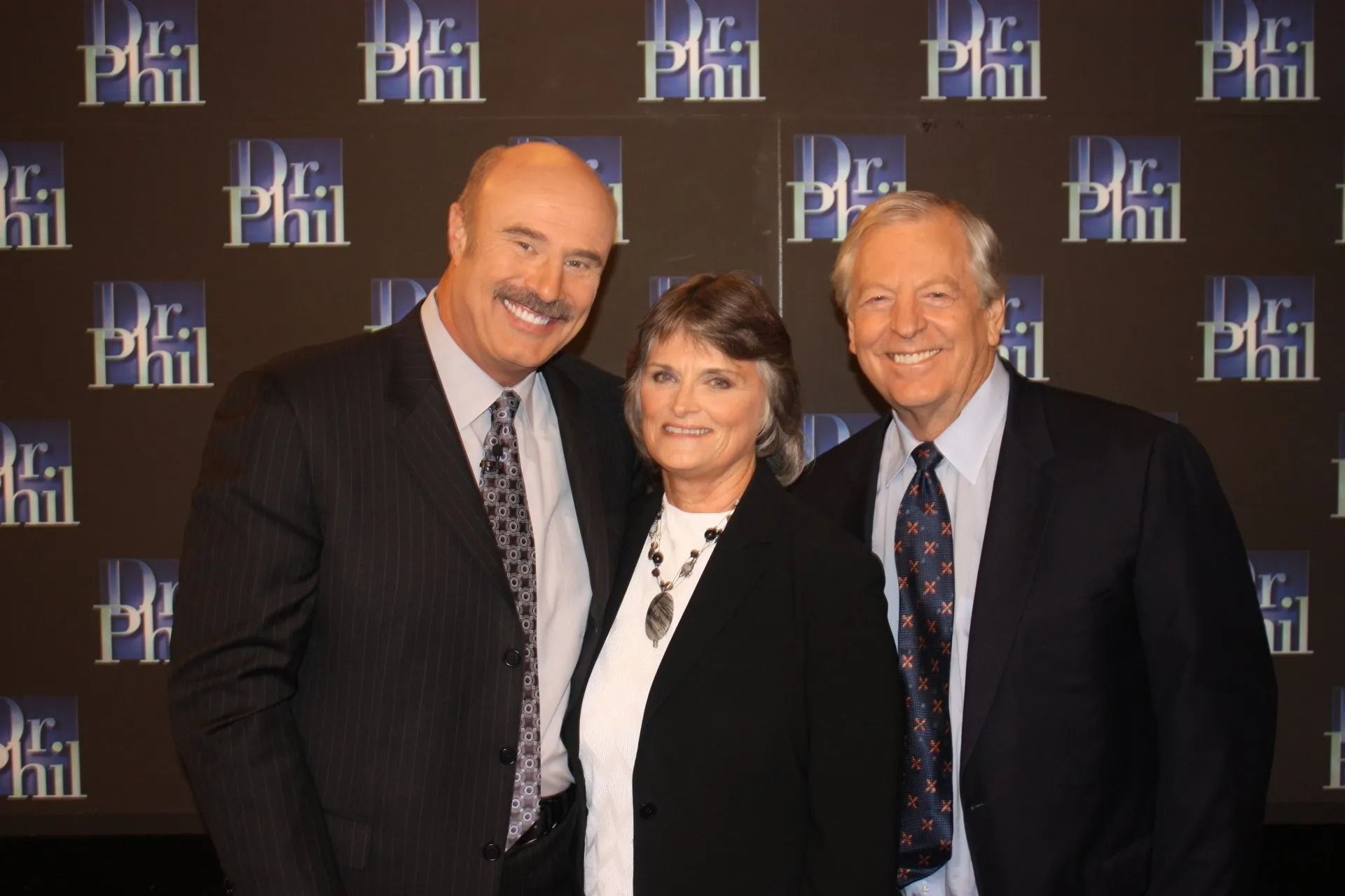 Three people posing at a Dr. Phil event in front of a Dr. Phil backdrop