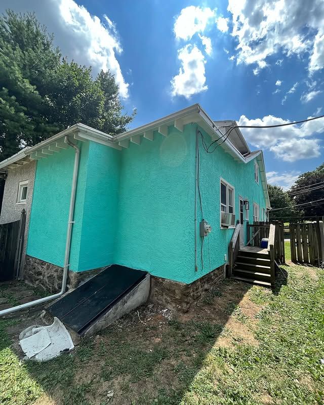 A green house with stairs leading up to it is sitting on top of a lush green field.