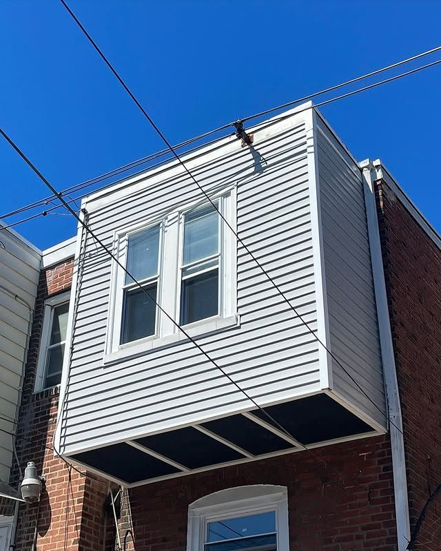 A brick building with a white siding and a window on the side.