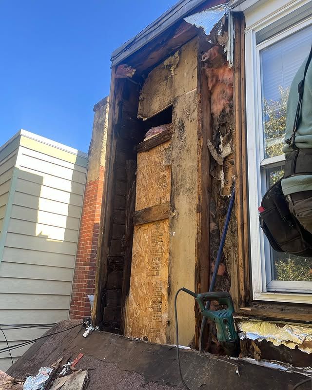 A person is working on the side of a house with a hammer.