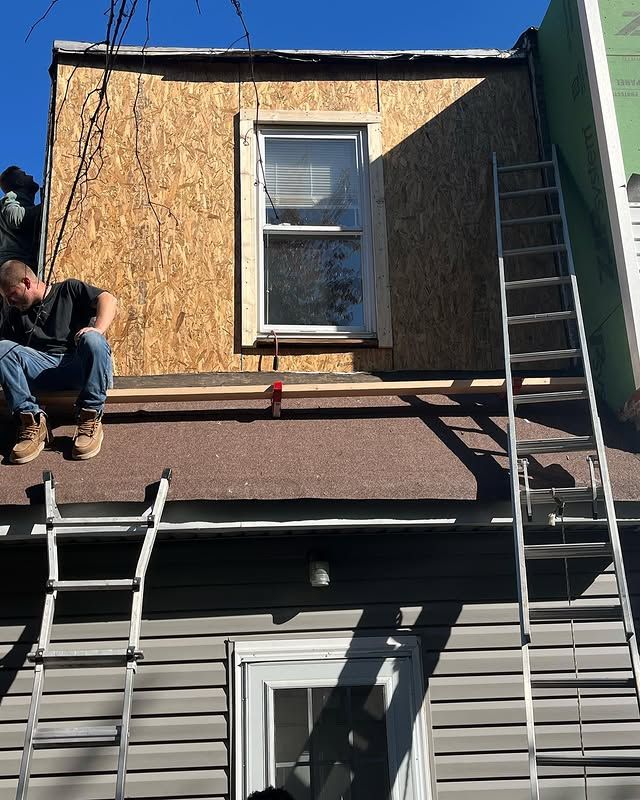 A man is sitting on the roof of a house with a ladder.