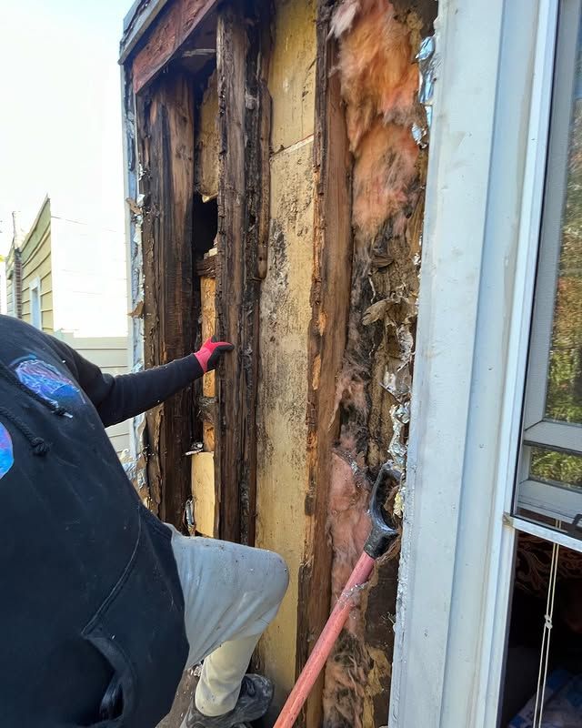 A man is holding a shovel and pointing at a hole in a wall.