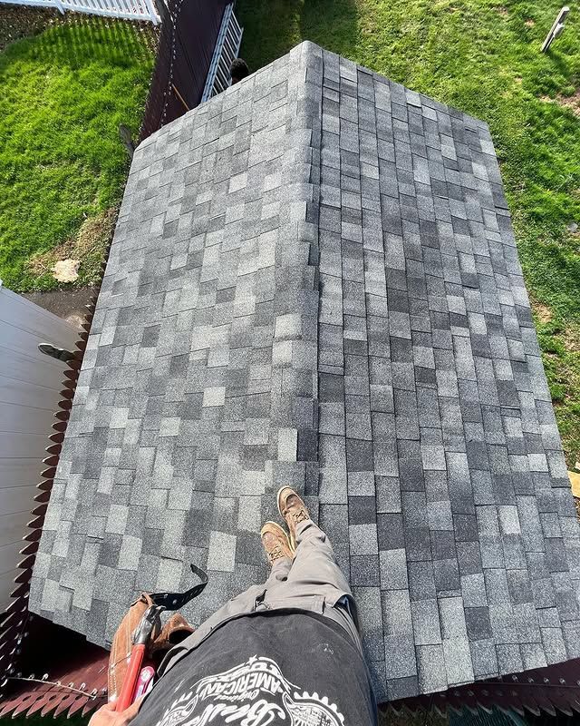 A man is standing on top of a roof with a hammer.