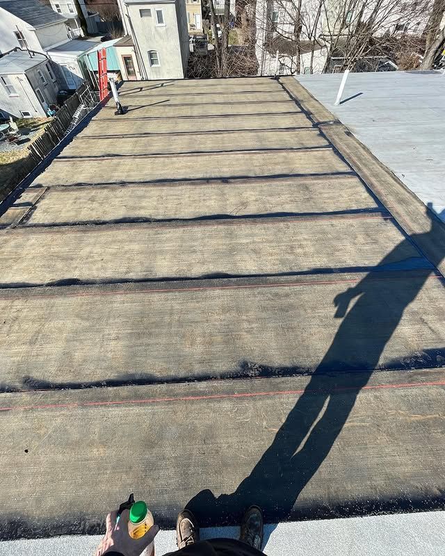 A person is standing on top of a roof with a bottle of liquid in their hand.