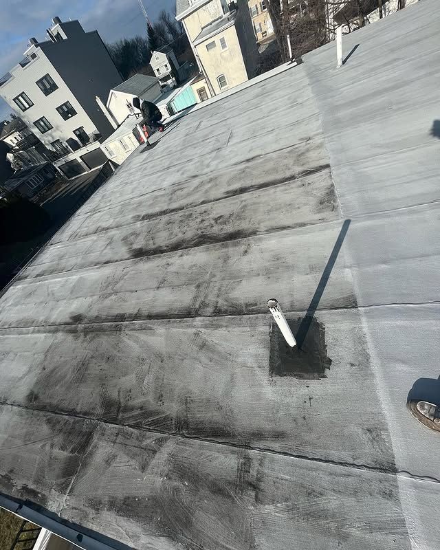 A roof with a pipe on it and a few buildings in the background.