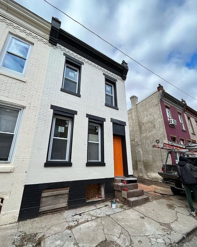 A white brick building with black trim and an orange door is being painted.