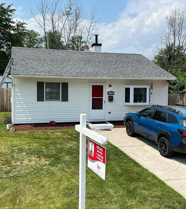 A white house with a blue car parked in front of it and a for sale sign.
