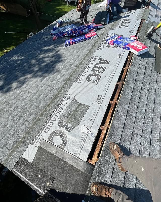 A person is standing on a roof with a piece of roofing material on it.