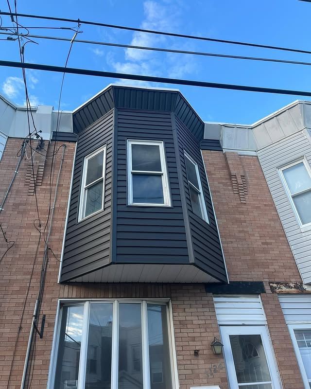 A brick building with a bay window and a black siding