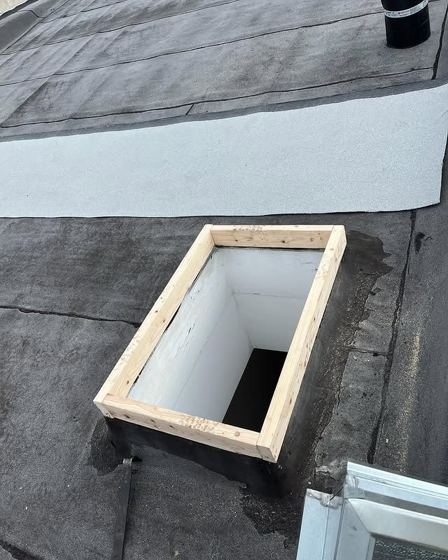 A skylight is sitting on top of a roof next to a window.