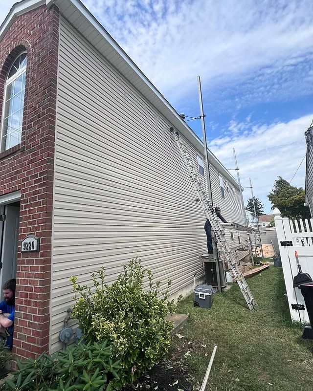 A man is painting the side of a house with a ladder.