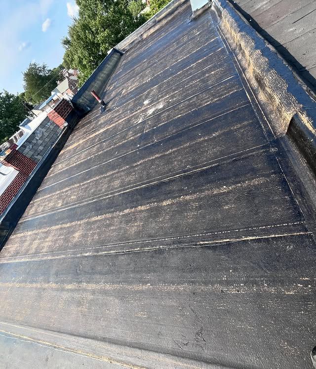 A close up of a black roof with a chimney in the background.
