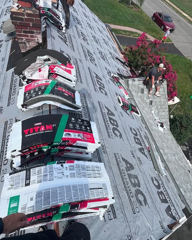 A person is standing on top of a roof holding a bag of abc shingles.