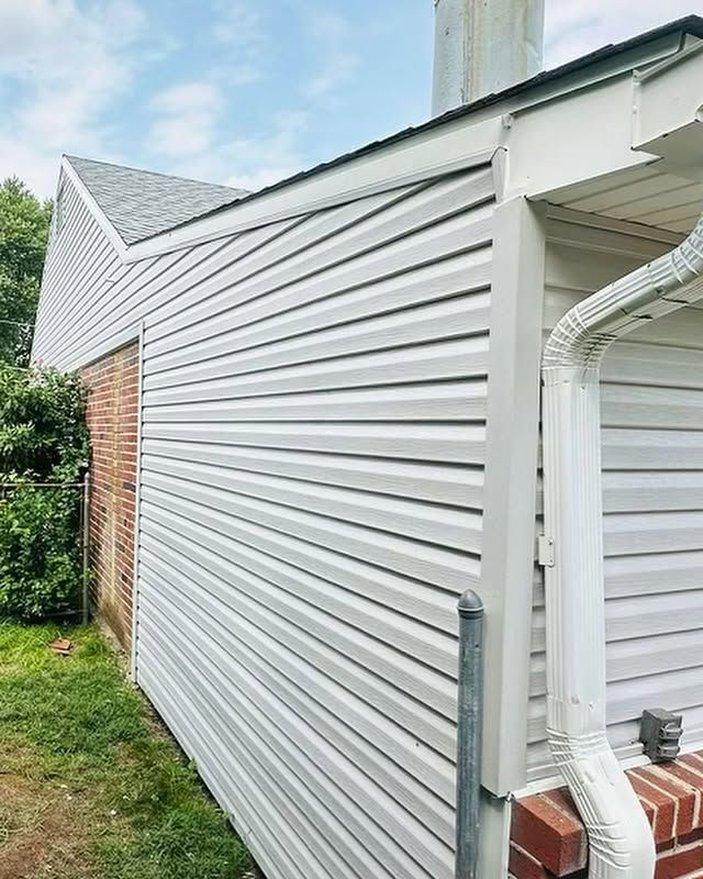 The side of a house with white siding and a drainpipe.
