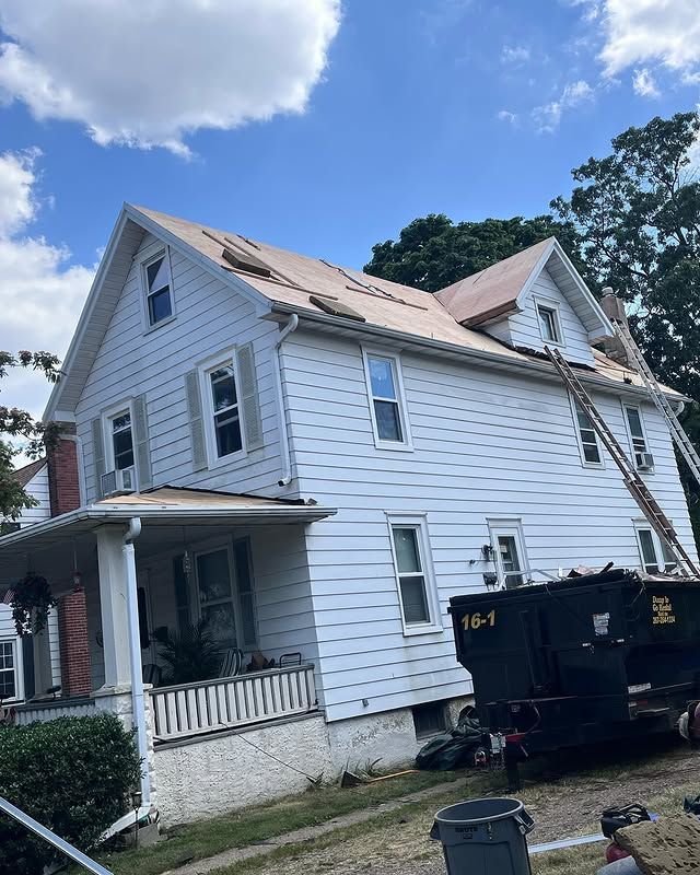 A white house with a roof being installed and a dumpster in front of it.