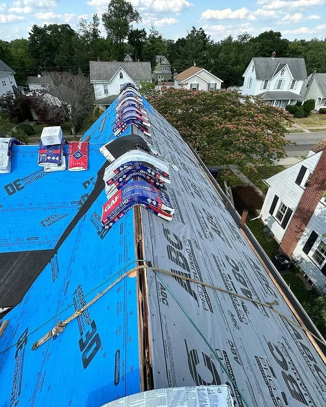 The roof of a house is being covered with a blue tarp.