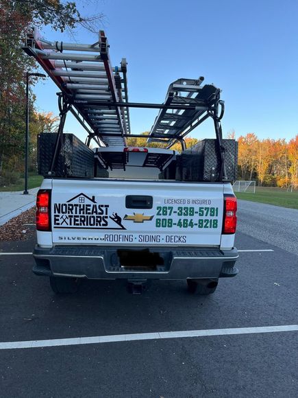 A white truck with a ladder rack in the back is parked on the side of the road.