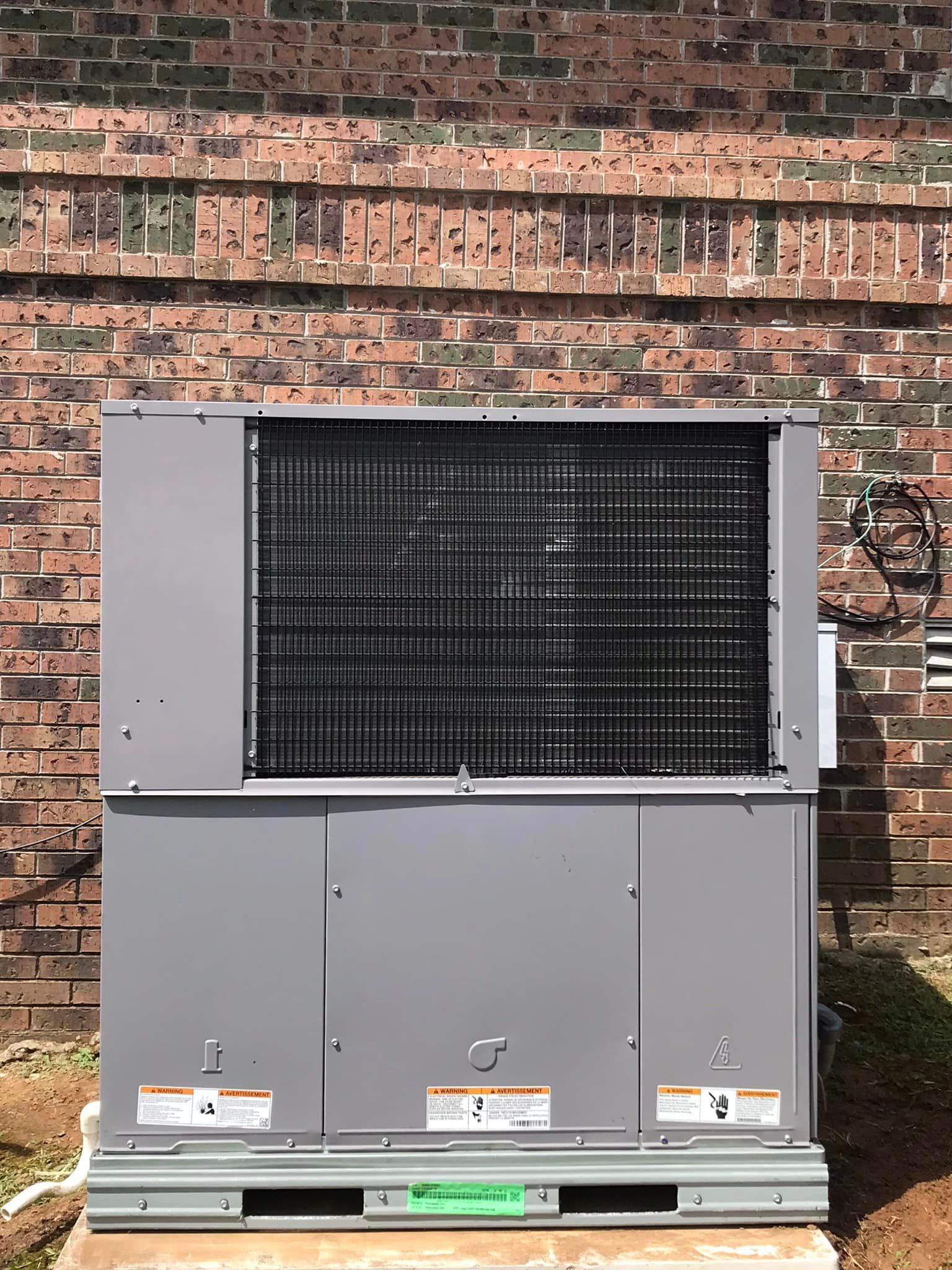 A large air conditioner is sitting on a pallet in front of a brick wall.