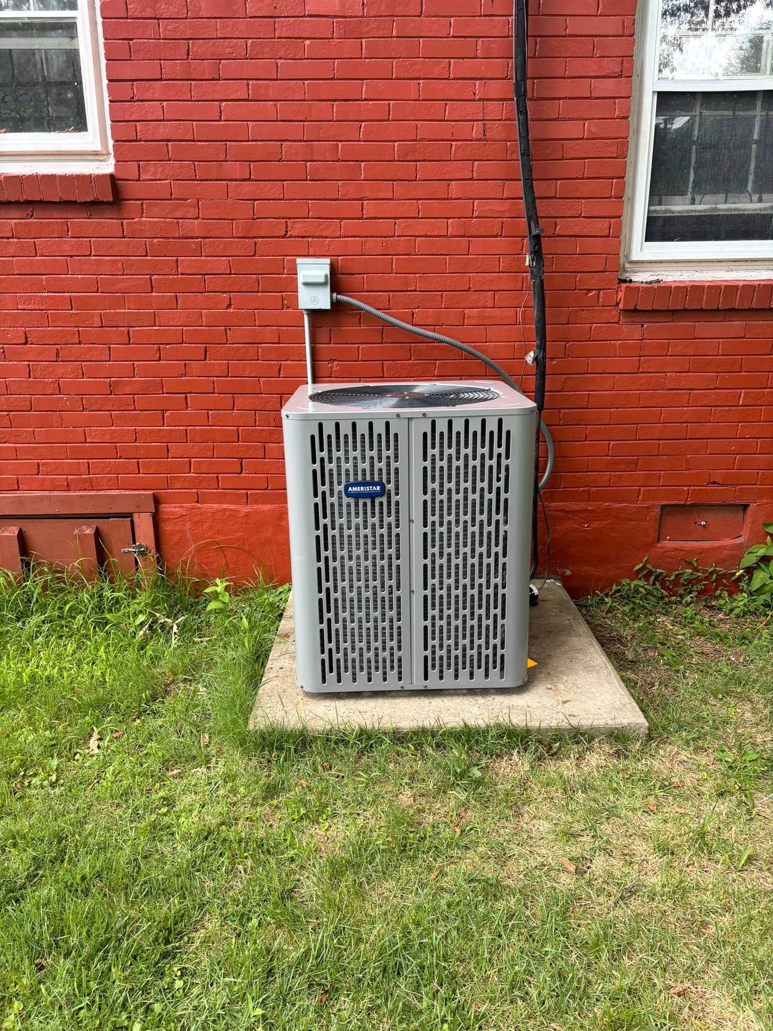 An air conditioner is sitting on the side of a red brick building.
