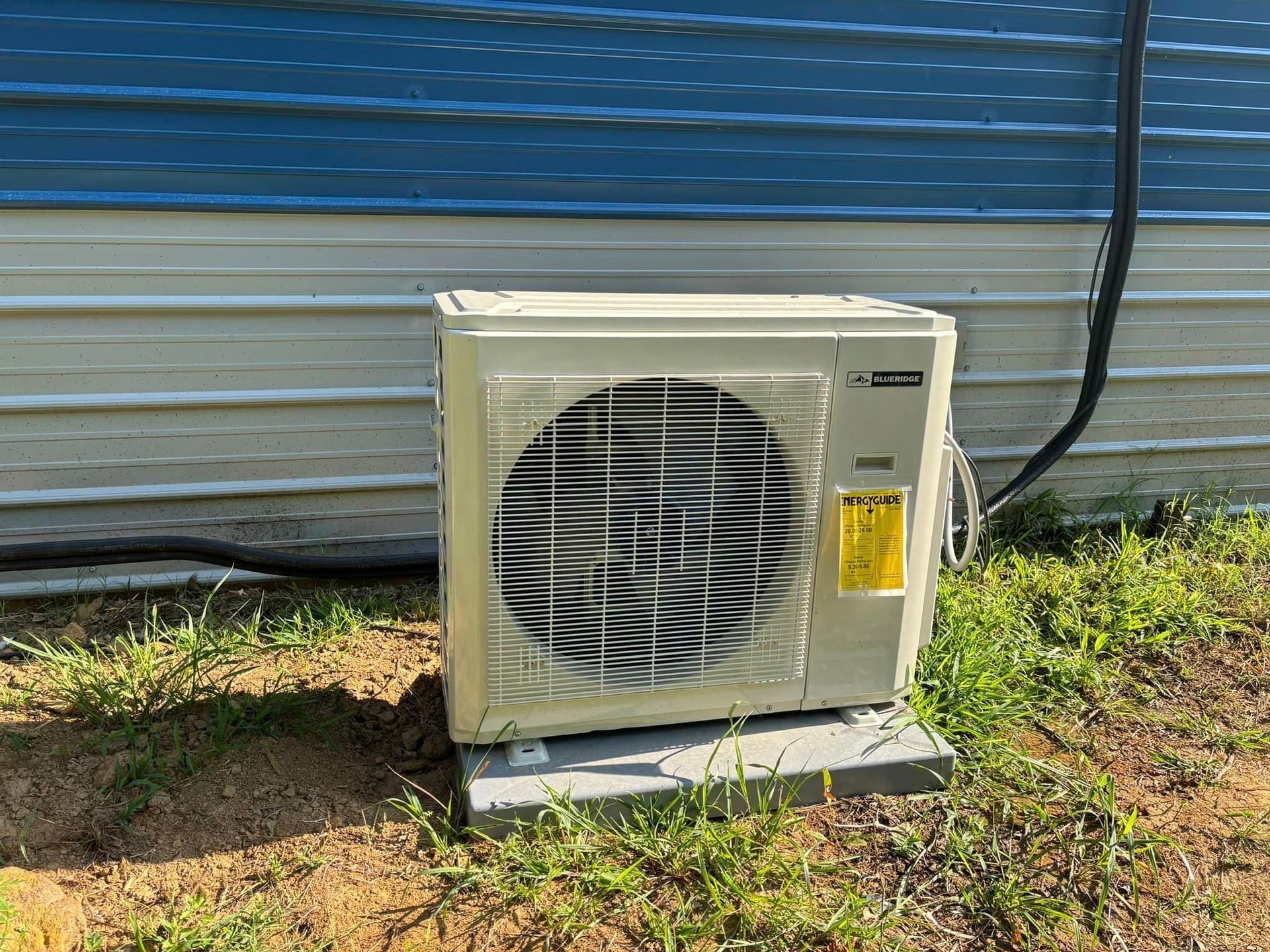 A white air conditioner is sitting in the grass next to a blue building.