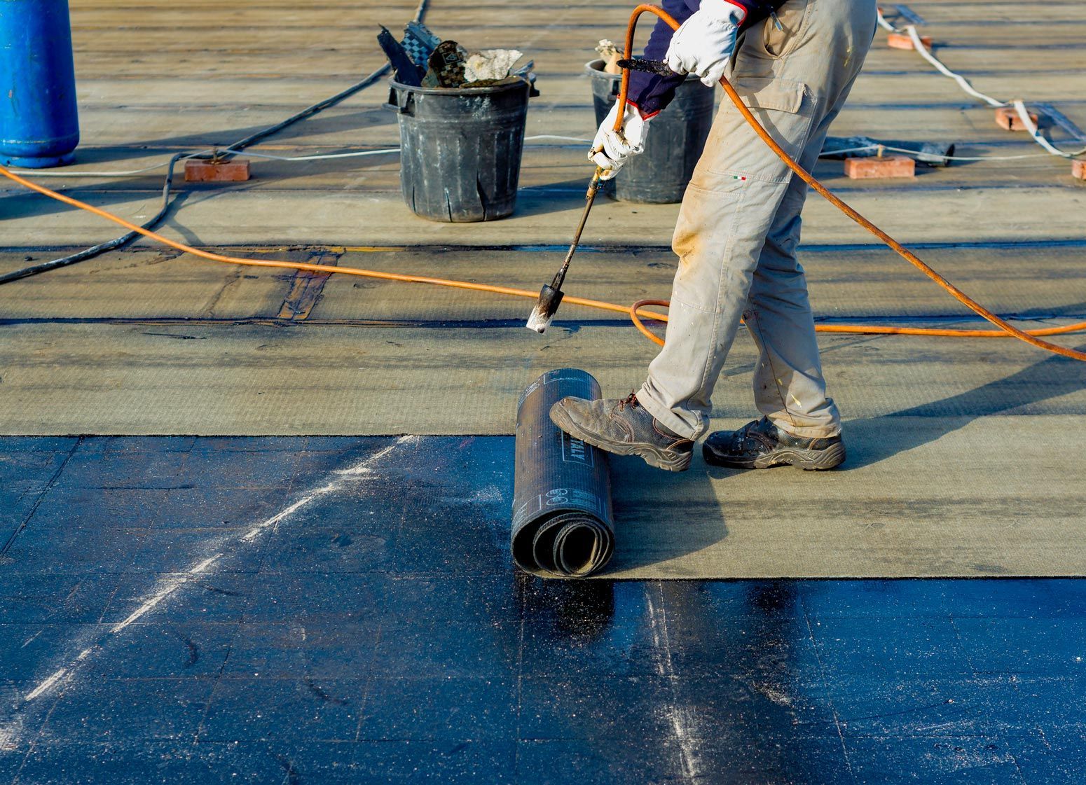 A man is rolling a roll of asphalt on a roof.