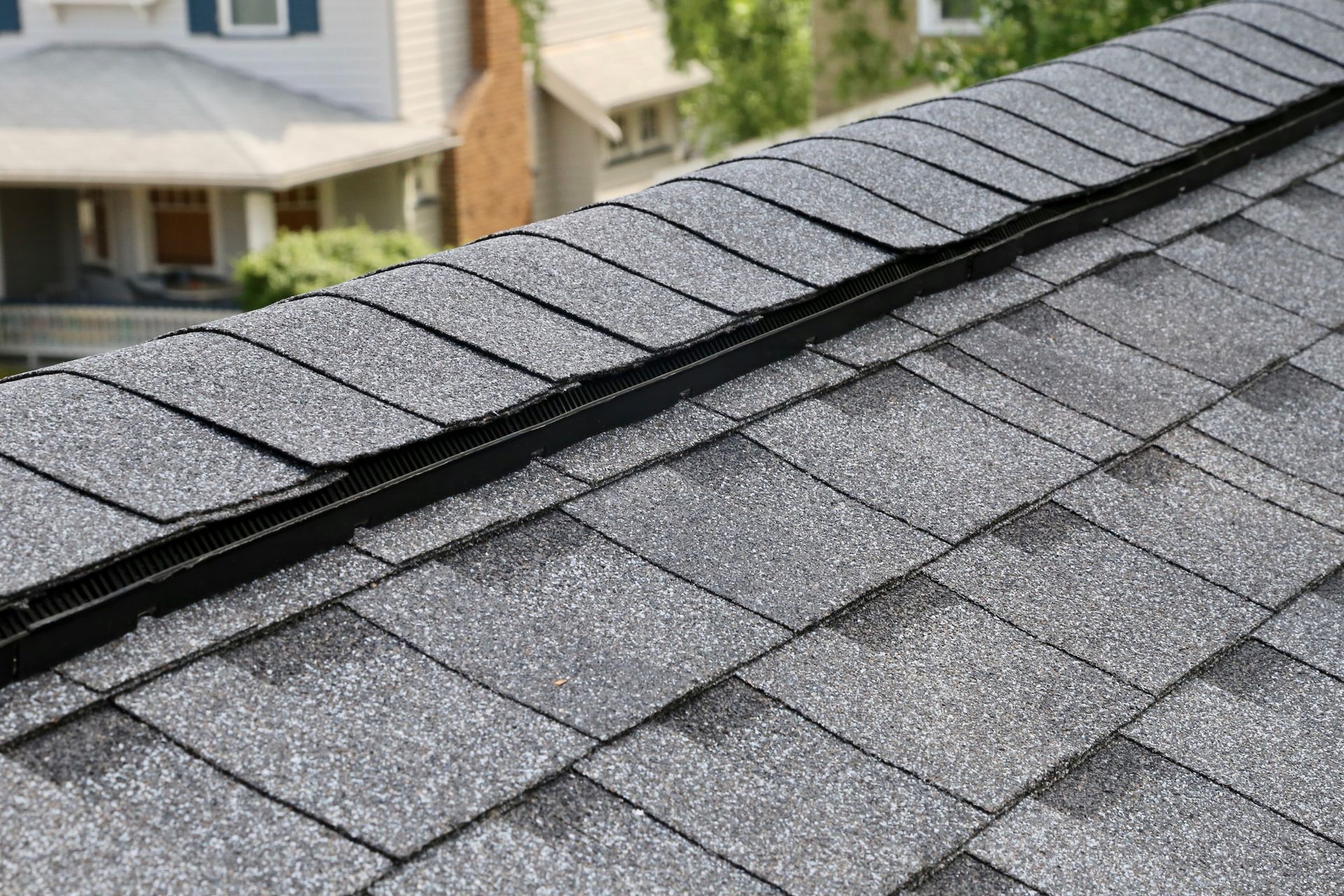 Close-up of a gray shingle roof with a valley where two roof sections meet, possibly damaged.