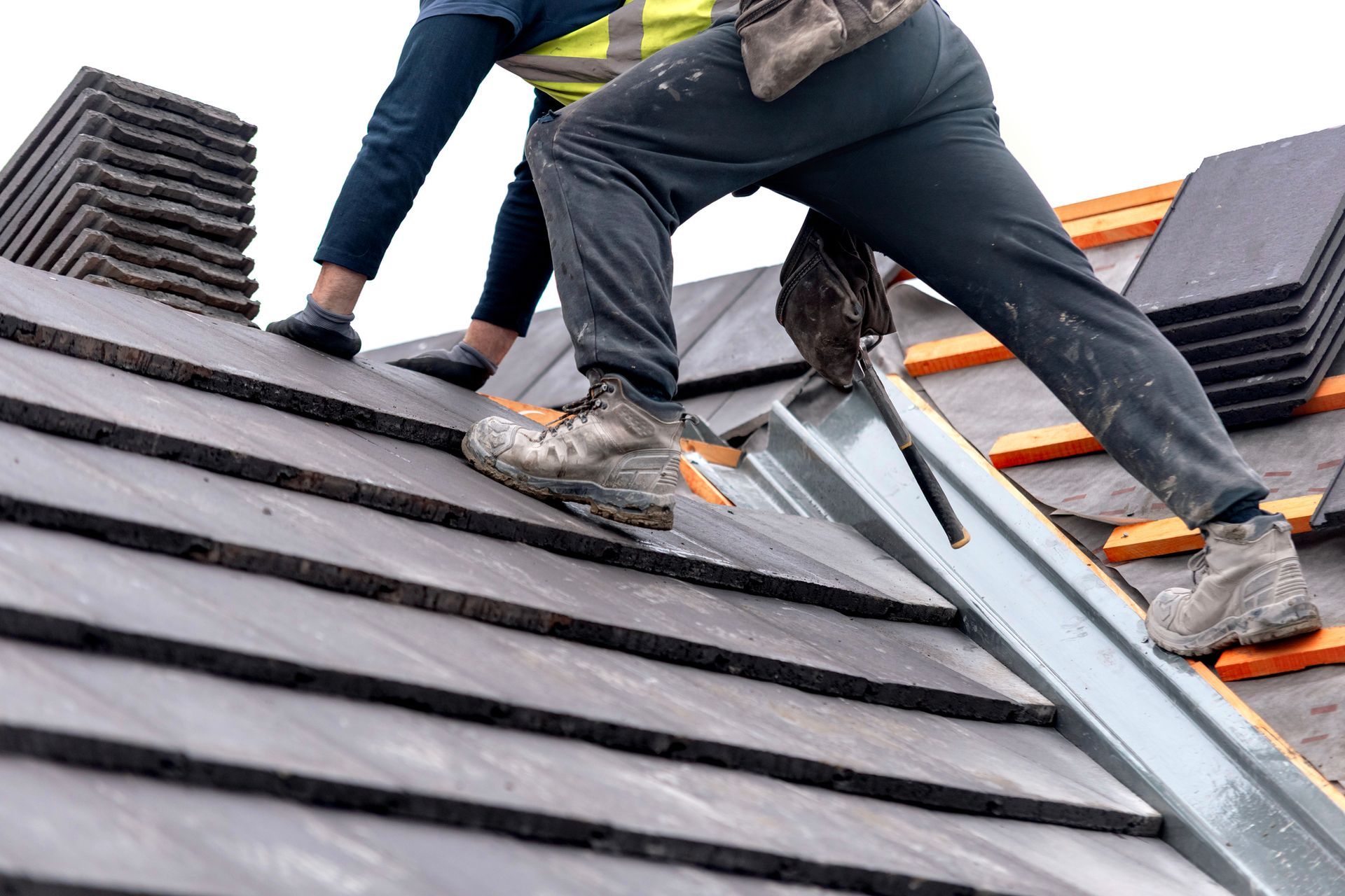 A roofer carefully places roof tiles on a sloped surface while standing on top of a roof. A roofer carefully places roof tiles on a sloped surface while standing on top of a roof.