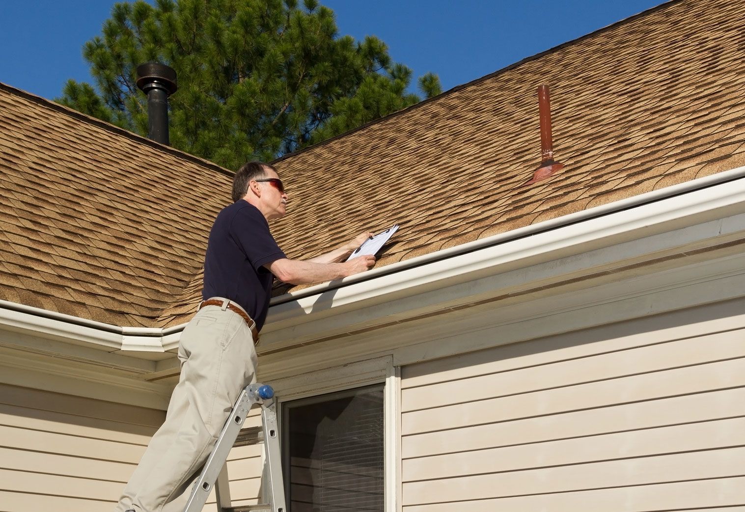 A man standing on a ladder looking at the roof of a house
