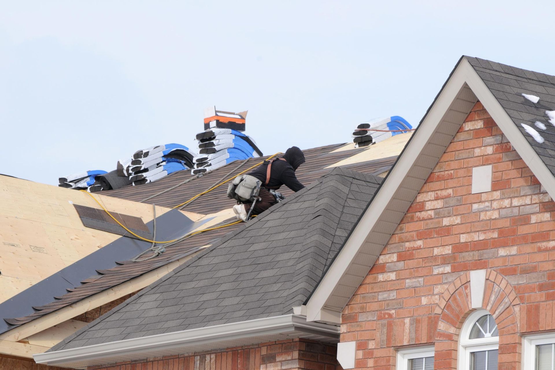 A man is working on the roof of a brick house.
