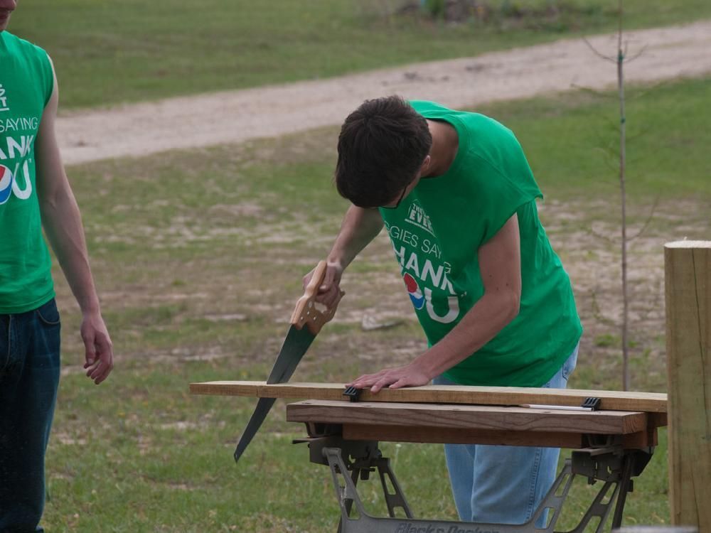 A man in a green shirt is cutting a piece of wood