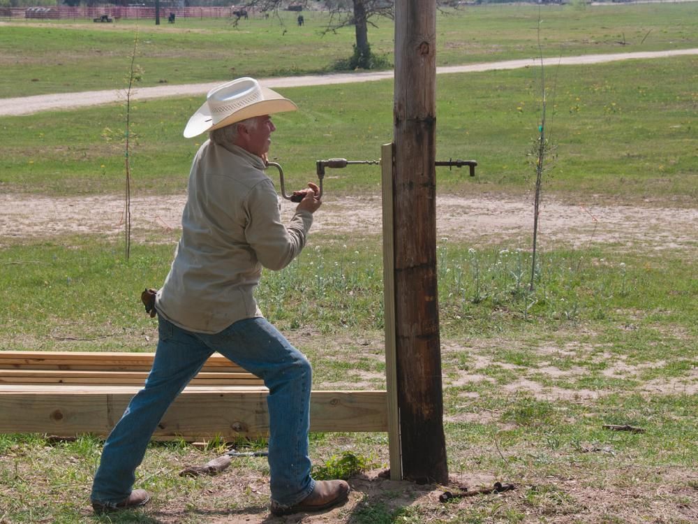 A man in a cowboy hat is working on a wooden post