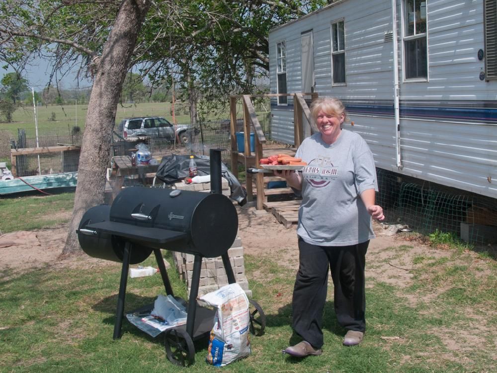 A woman in a gray shirt is standing in front of a grill