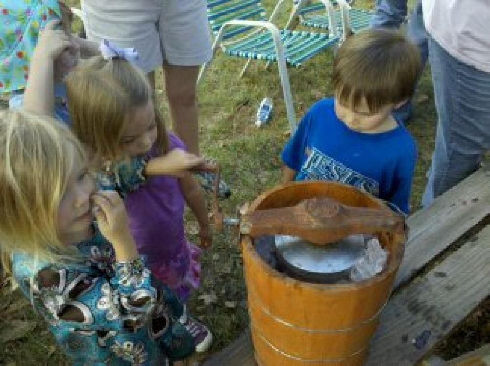 A group of children are standing around a wooden bucket of ice cream.