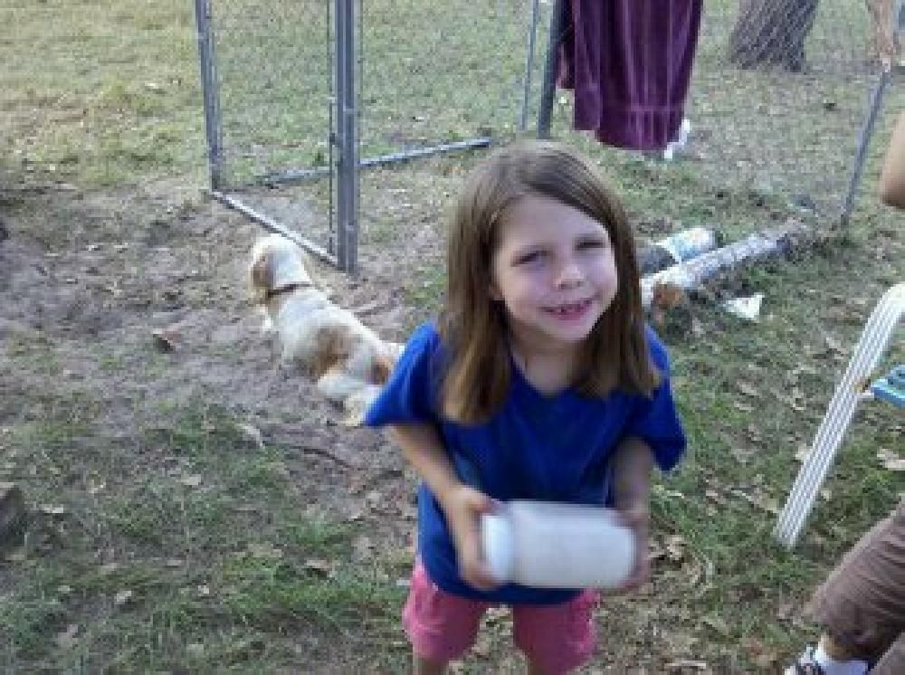 A little girl in a blue shirt is holding a white bottle