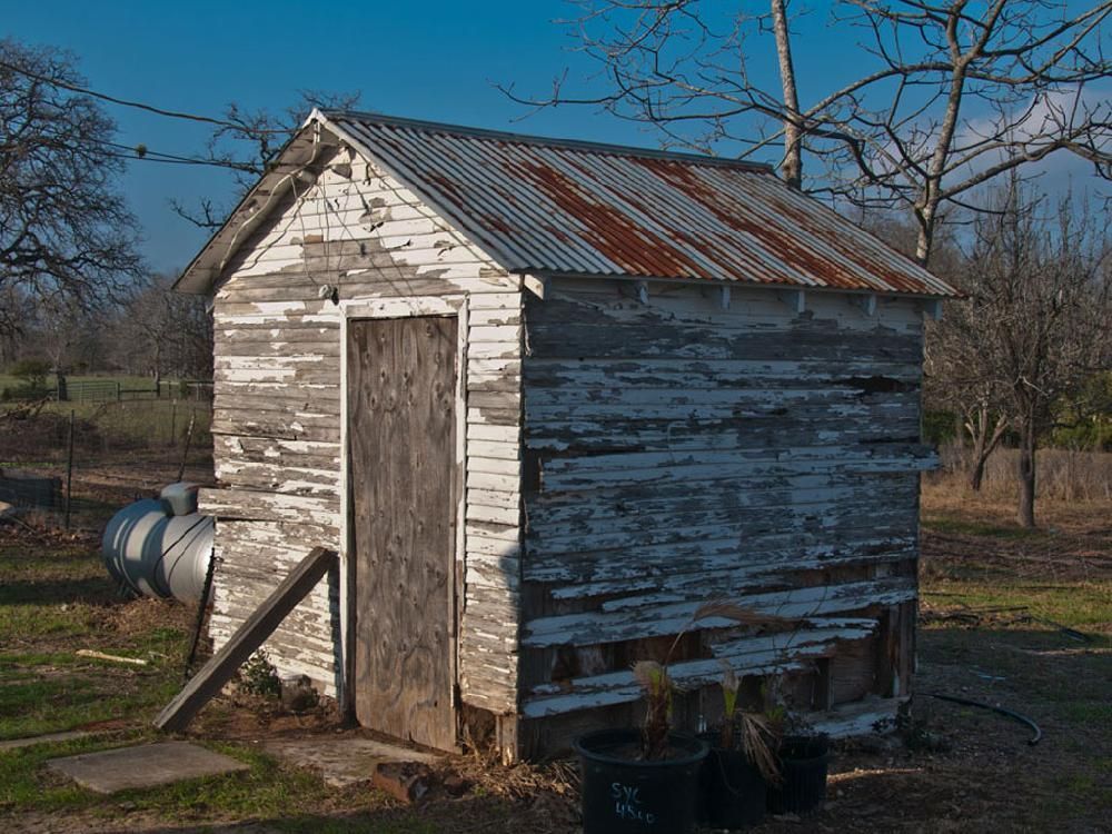 A small white shed with a rusty tin roof