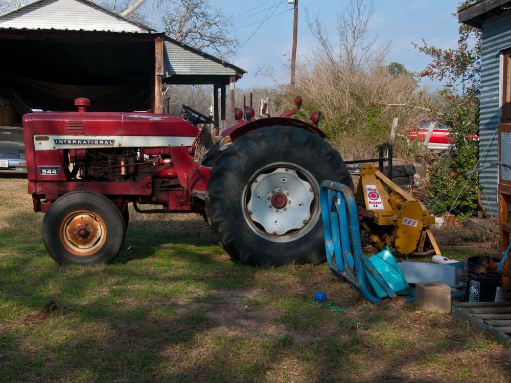 A red tractor is parked in the grass in front of a garage