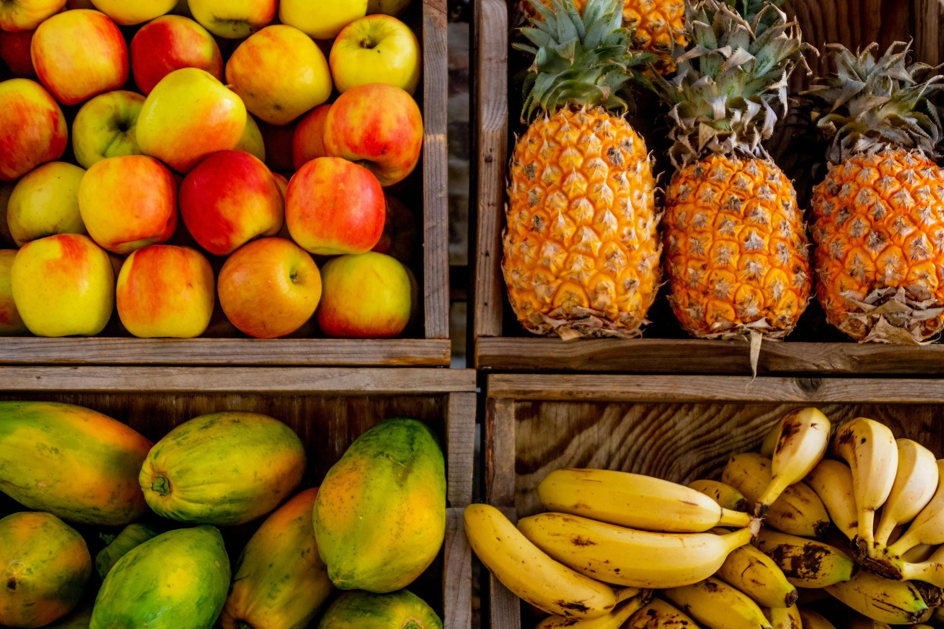 Pineapples , apples , papayas , and bananas are in wooden crates.