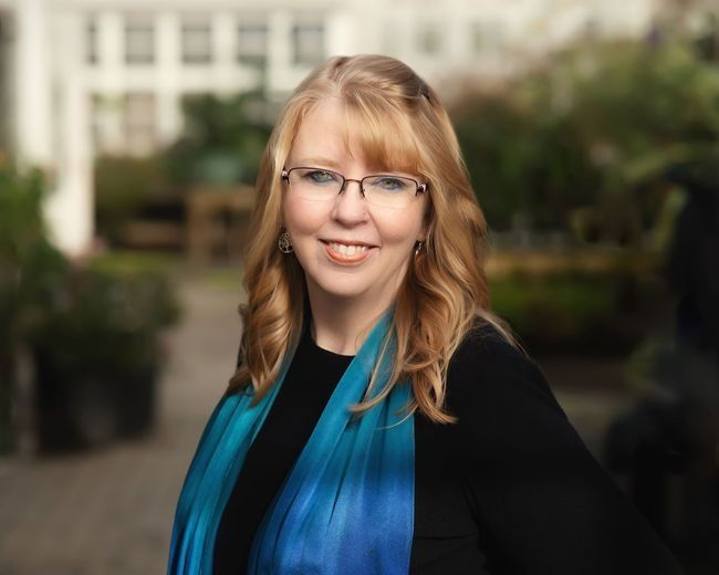A woman wearing glasses and a blue scarf is smiling for the camera.