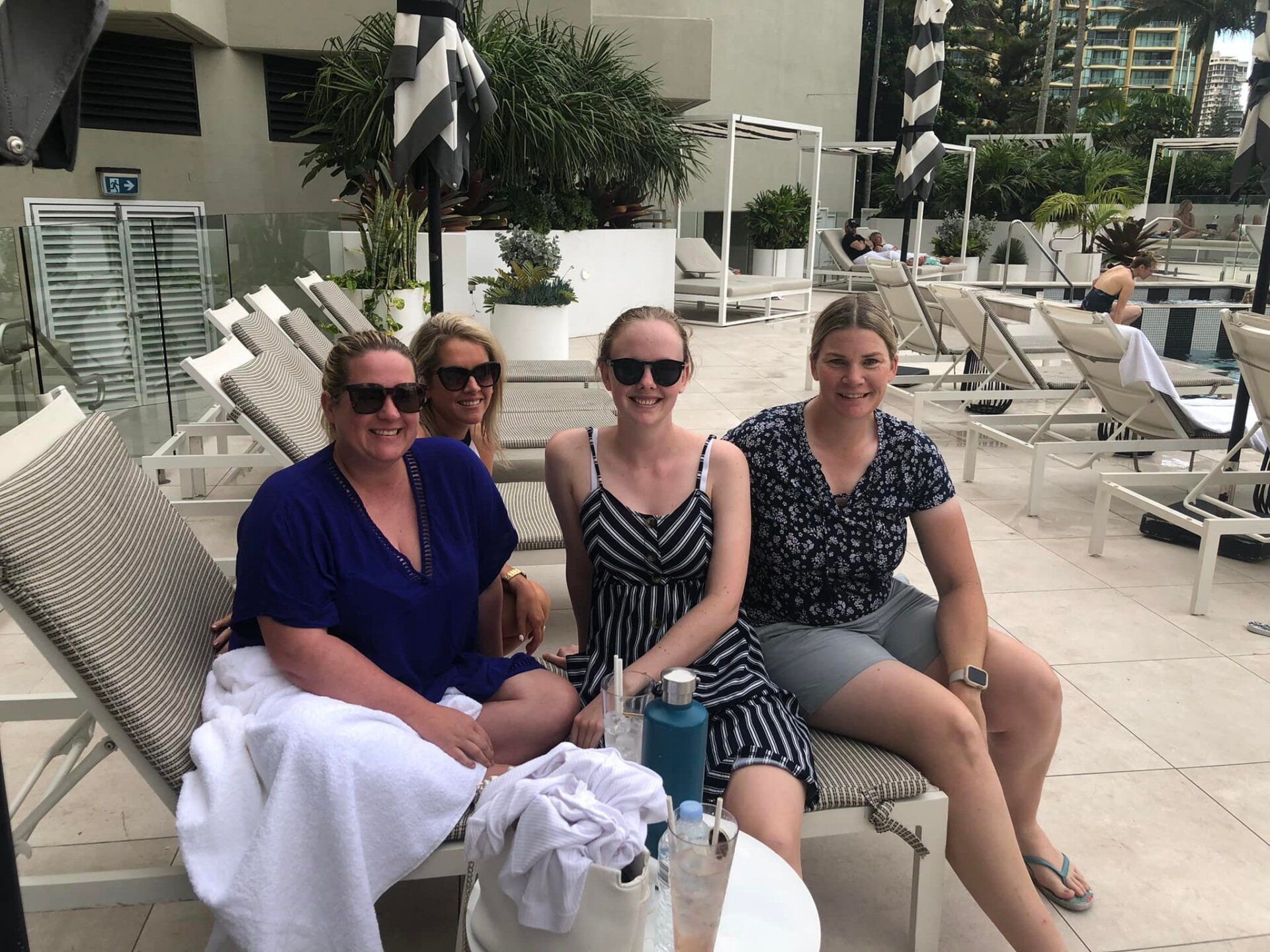 4 ladies sitting on sun lounges by the pool at the gold coast smiling.
